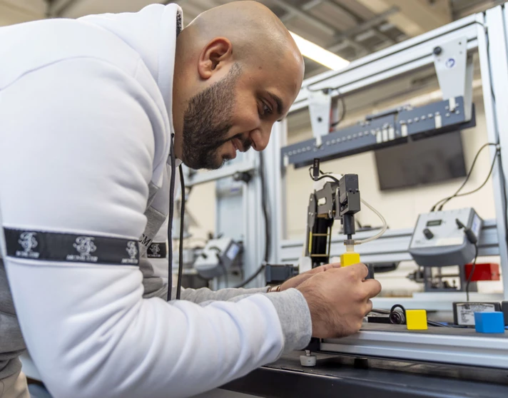 Student operating a robotic arm, carefully placing a yellow block on a conveyor system as part of an automation project Student operating a robotic arm, carefully placing a yellow block on a conveyor system as part of an automation project